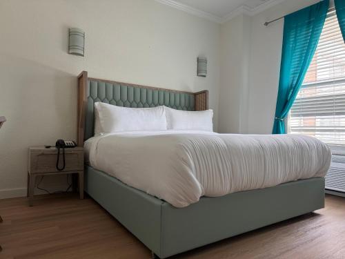 a bedroom with a large bed with white sheets and blue curtains at Athens Hotel & Suites in Houston