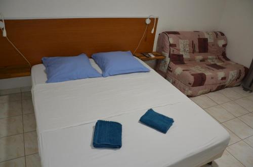 a white bed with blue pillows and a chair at La suite Corossol in Gros-Morne