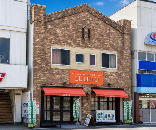 a brick building with red awnings on a street at Guesthouse LuLuLu 無料朝食&夕食ｶﾚｰ付き ﾛｰｿﾝ隣 街まで電車8分 in Kochi