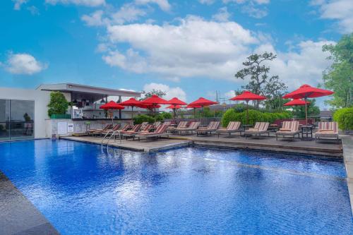 a swimming pool with chairs and red umbrellas at Sevn Legian in Legian