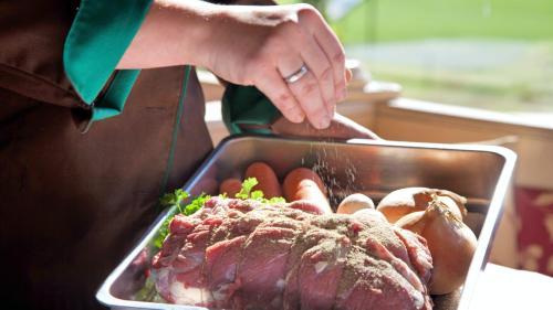 a woman is reaching into a tray of meat and vegetables at Landgasthof Entenwirt Tarsdorf in Tarsdorf
