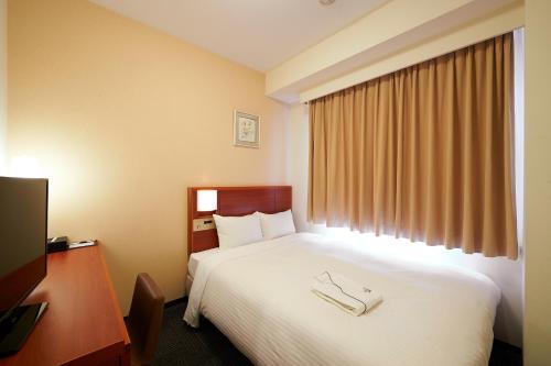 a hotel room with a bed and a desk and a television at Sotetsu Fresa Inn Fujisawa Shonandai in Fujisawa