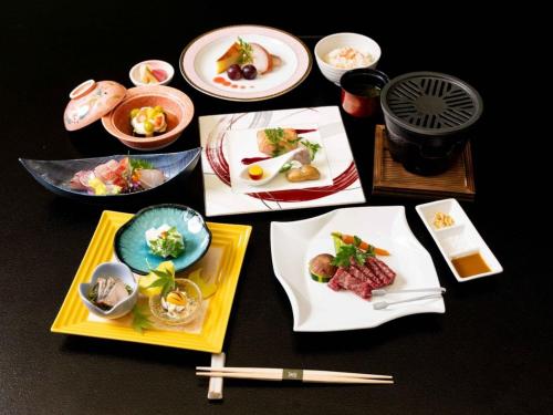 a table topped with plates of food and chopsticks at Izukogen Hotel Itsutsuboshi in Ito
