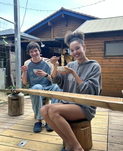 two young people sitting on a deck eating food at ログハウス1棟貸し,持込み自由,サウナ,露天風呂にバーべキュウや薪割り,ソーメン流しに収穫体験が楽しめます in Kashima