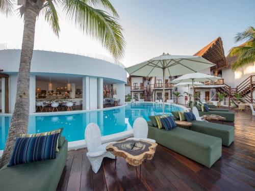a resort pool with couches and tables and palm trees at Villas HM Palapas del Mar in Holbox Island