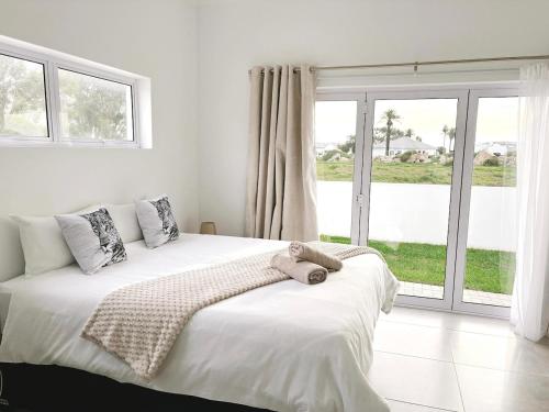 a white bedroom with a large bed and a window at Villa Jabulani in Stompneusbaai