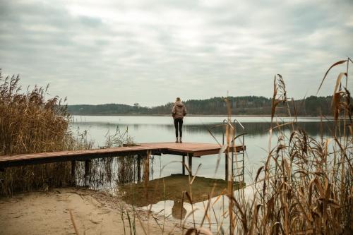 a person standing on a wooden dock near a lake at Rajsco - domek nad Jeziorem Budzisławskim in Tręby Stare