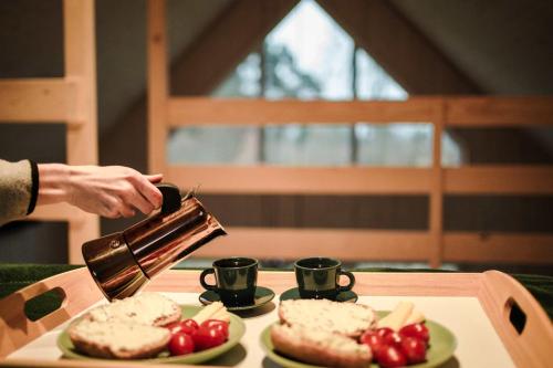 a person pouring coffee into cups on a table at Rajsco - domek nad Jeziorem Budzisławskim in Tręby Stare