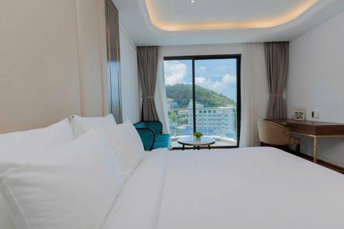 a bedroom with a white bed and a desk and a window at Oyster Bay Vũng Tàu - Seaside Pool Escape in Vung Tau