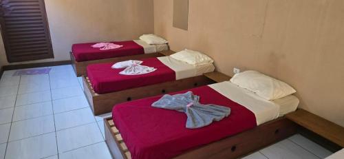 three beds in a room with pink sheets at Pousada Catuaí in Siqueira Campos