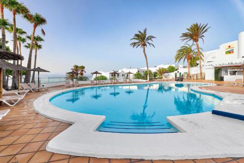 ein großer Swimmingpool mit Palmen und dem Meer in der Unterkunft Hotel THB Flora in Puerto del Carmen