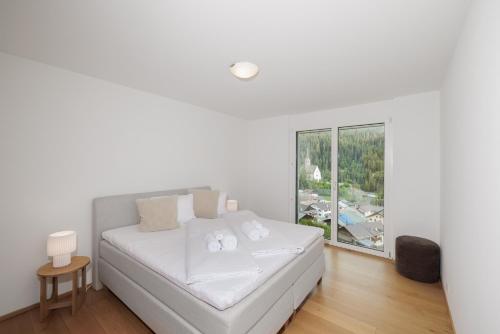 a white bedroom with a bed and a large window at Chasa Miramunt 2 in Scuol
