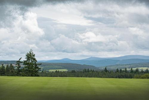a green field with trees and mountains in the background at Douneside House in Tarland