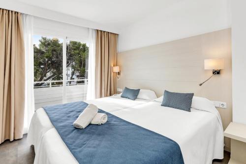 two beds in a hotel room with towels on the bed at HSM Lago Park in Playa de Muro