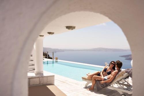 two women sitting on chairs next to a swimming pool at Homeric Poems in Fira