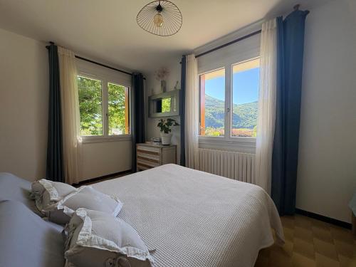 a bedroom with a white bed and two windows at Le petit gîte in Saint-Étienne-le-Laus