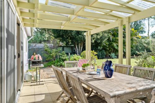 a patio with a wooden table and chairs under a pergola at Sugar Shack Currarong in Currarong