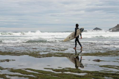 a man walking on the beach with a surfboard at Itsasmin Ostatua in Elanchove
