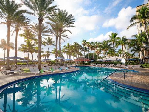 a swimming pool with chairs and palm trees at Ocean Pointe Resort One-Bedroom Villa in Palm Beach Shores