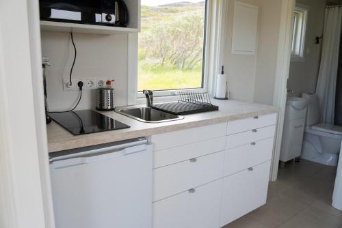 a kitchen with white cabinets and a sink and a window at Hvammur 6 with private hot tub in Hafnarhólmur