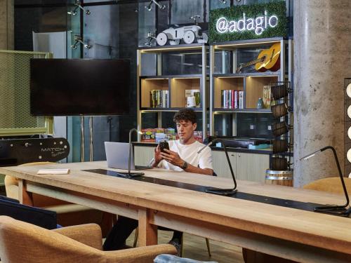 a man sitting at a table looking at his cell phone at Aparthotel Adagio London Brentford in Brentford