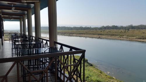 a row of chairs sitting on a porch next to a river at Jungle Wildlife Camp in Sauraha