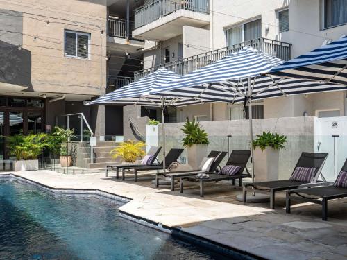 a pool with lounge chairs and umbrellas next to a building at The Sebel Byron Bay in Byron Bay