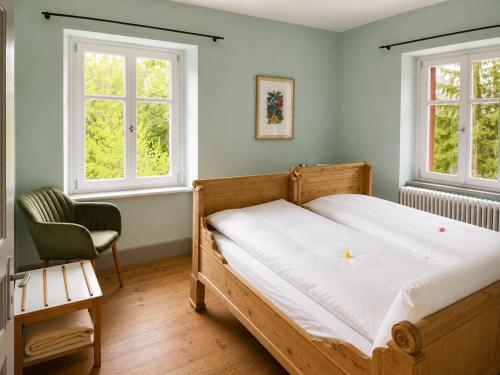 a bedroom with a bed and a chair and two windows at Gasthaus Crestasee in Flims
