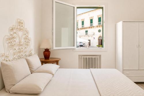 a white bedroom with a white bed and a window at Colonna Apartment Ostuni in Ostuni