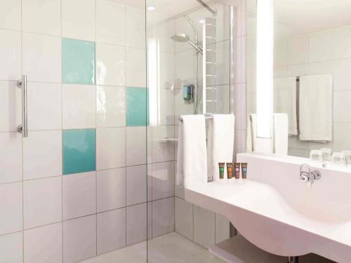 a white bathroom with a sink and a shower at Novotel Nürnberg am Messezentrum in Nuremberg