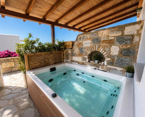 a hot tub in a patio with a stone wall at Thea Suites Naxos in Agios Prokopios