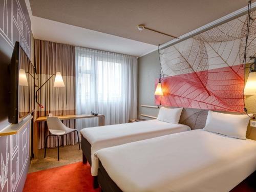 a hotel room with two beds and a desk at ibis Nürnberg City am Plärrer in Nuremberg