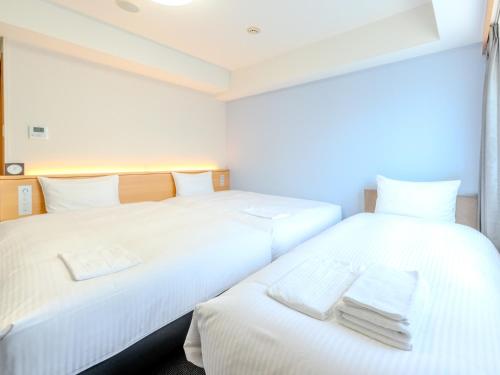 two beds in a room with white sheets and towels at Richmond Hotel Hakata Ekimae in Fukuoka