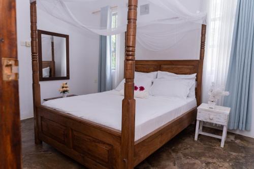 a bedroom with a wooden four poster bed with a mirror at Auregi Villas in Diani Beach