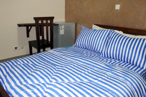 a bed with a blue and white striped comforter and a chair at Maison Babacar TOURE in Dakar