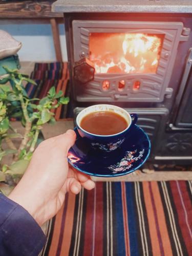 a person holding a cup of coffee in front of an oven at Geyikli Konak in Mudurnu