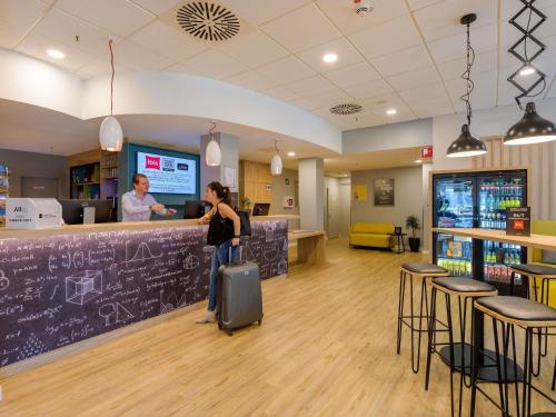 a woman with a suitcase standing at a bar in a store at ibis Hotel Frankfurt Messe West in Frankfurt