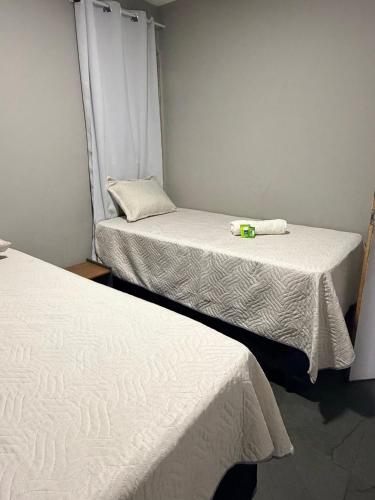two beds in a small room with white sheets at Apartamento Prático Completo in Goiânia