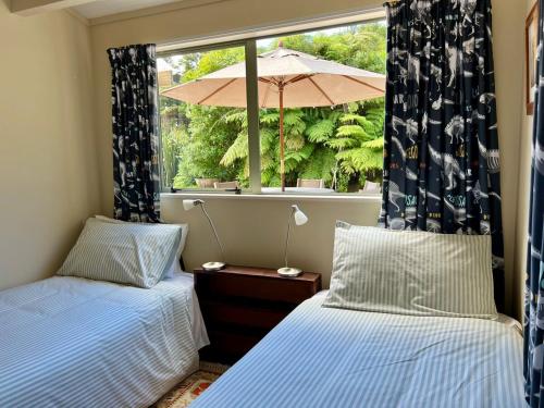 two beds in a room with a window with an umbrella at Secluded Bush Retreat in Hikuai