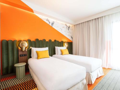 two beds in a hotel room with an orange wall at Mercure Shéhérazade Rabat in Rabat