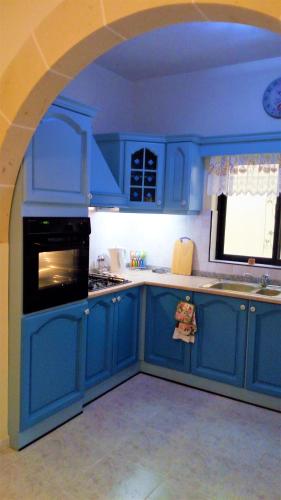 a blue kitchen with blue cabinets and a window at Peprina in Mġarr