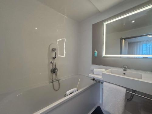 a bathroom with a tub and a sink and a mirror at Novotel Suites Rouen Normandie in Rouen