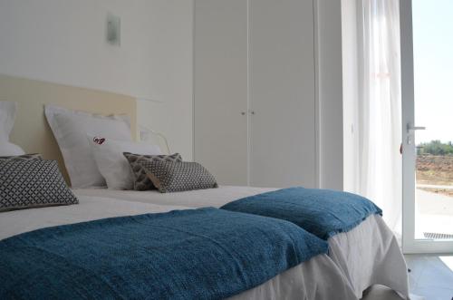 a bed with a blue blanket on it with a window at Entre Vinhas & Mar in Óbidos