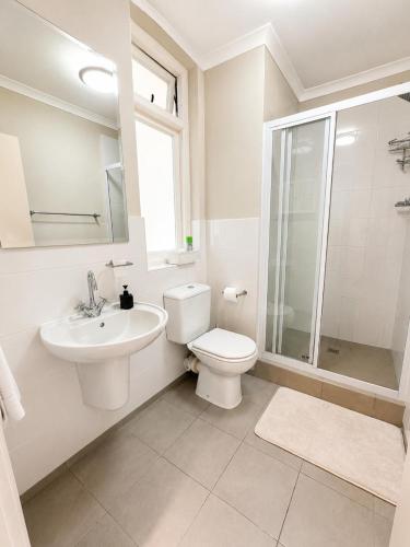 a white bathroom with a toilet and a sink at Muizenberg Surfers corner and Beach Paradise in Cape Town