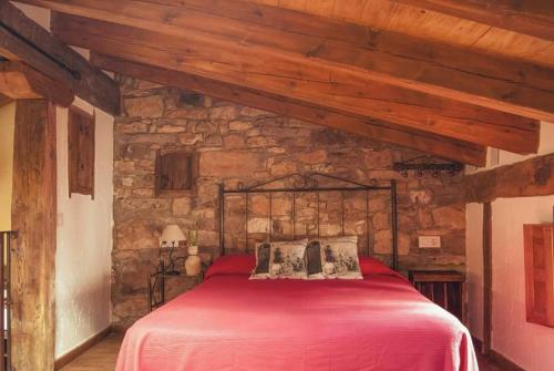 1 dormitorio con 1 cama roja en una pared de piedra en La Lagunilla, en Laguna del Marquesado