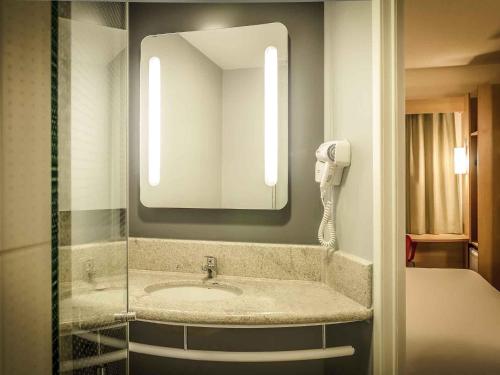 a bathroom with a sink with a mirror and a phone at Ibis Porto Alegre Assis Brasil - Estacionamento Gratuito para hospedes in Porto Alegre