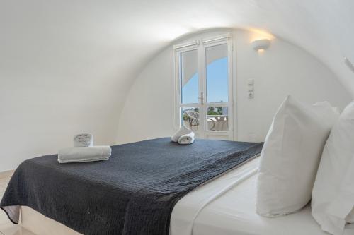 a white bedroom with a bed with a window at Bella Santorini Hotel in Perivolos