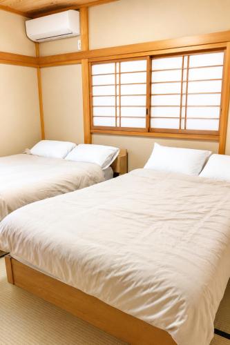 two beds in a room with two windows at A forest guesthouse with barbecue facilities in Nikko