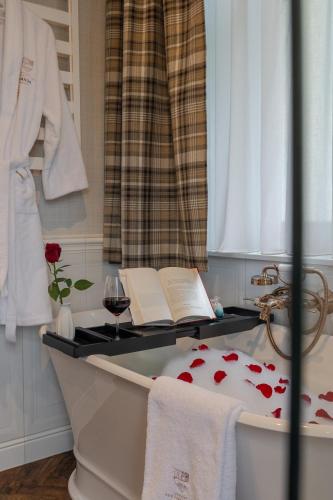 a bath tub with a book and a glass of wine at Wanda Luxury Boutique Hotel - tylko dla dorosłych in Szczawnica