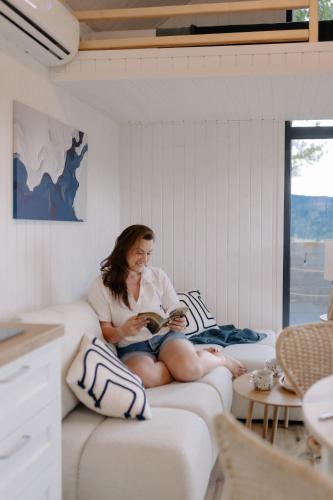 a woman sitting on a couch reading a book at Okno na Beskidy -domek NIEBO z balią , sauną i niesamowitym widokiem na góry in Maków Podhalański